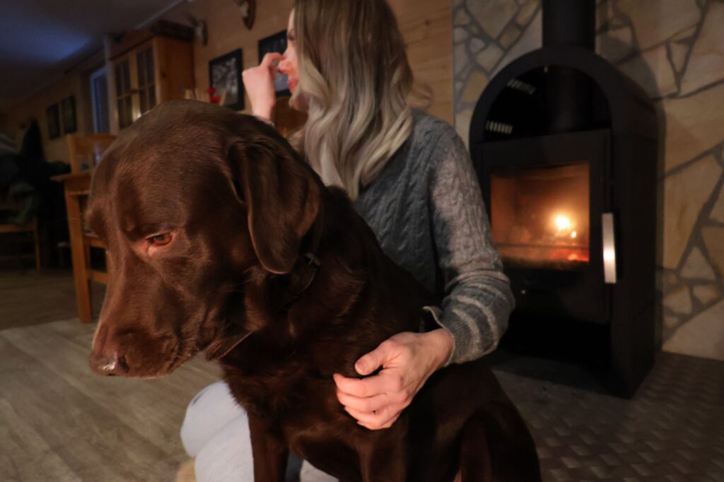 Frau mit Labrador am Kaminofen – Hund willkommen im Naturcamp Meyersgrund